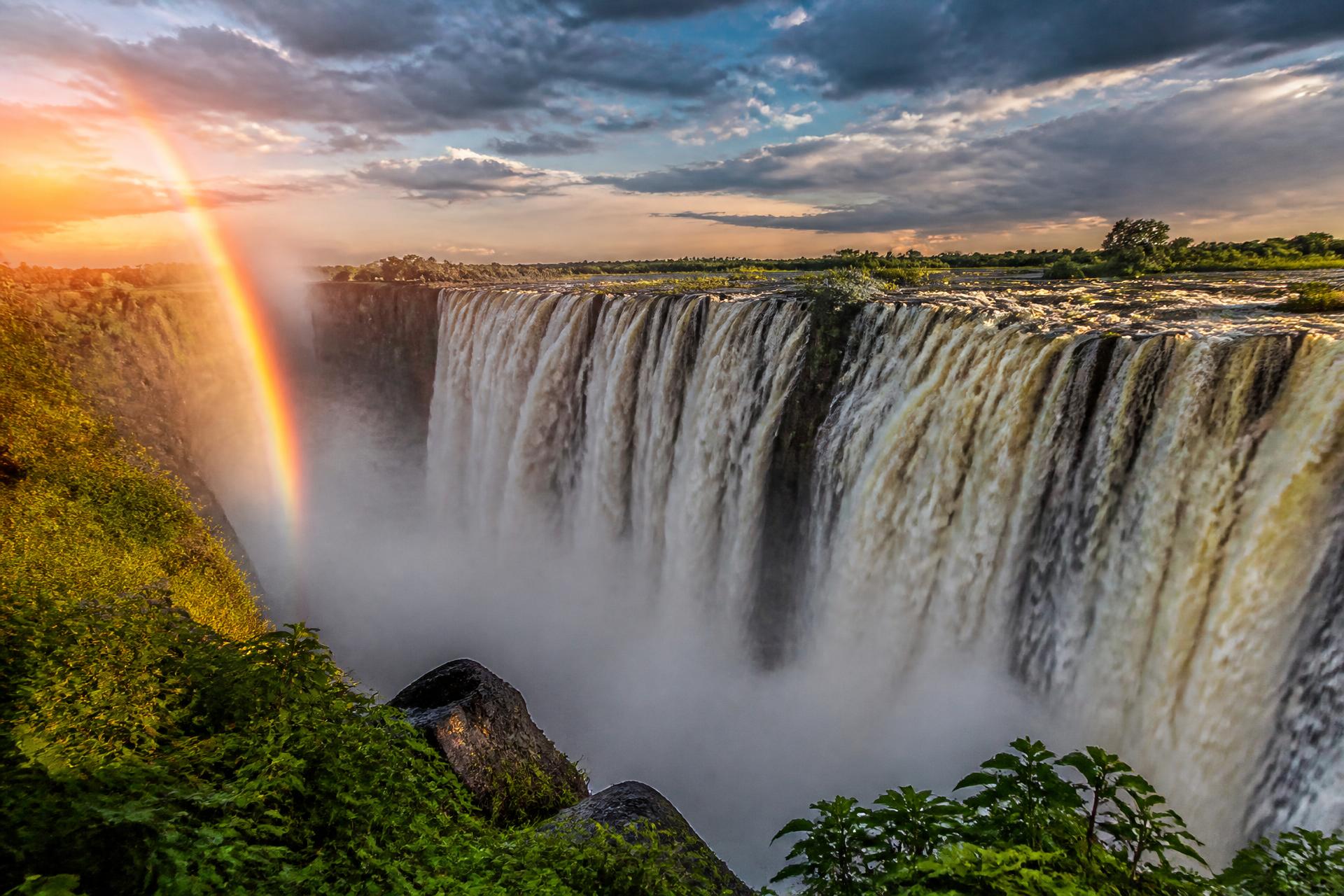 Victoria Falls in Zimbabwe with mist and a rainbow at golden hour